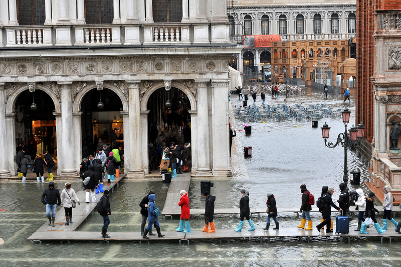 People walk on wooden boards set up as walk ways as high water floods St. Mark’s Square, in Venice, Italy, Friday, Feb. 6, 2015. AP Photo/Luigi Costantini